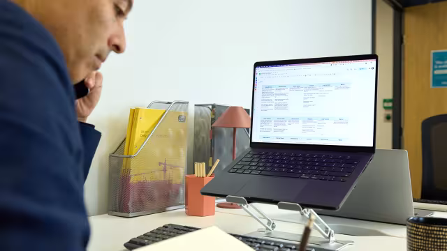 Person on a phone call while taking notes at a desk with a laptop on a stand.