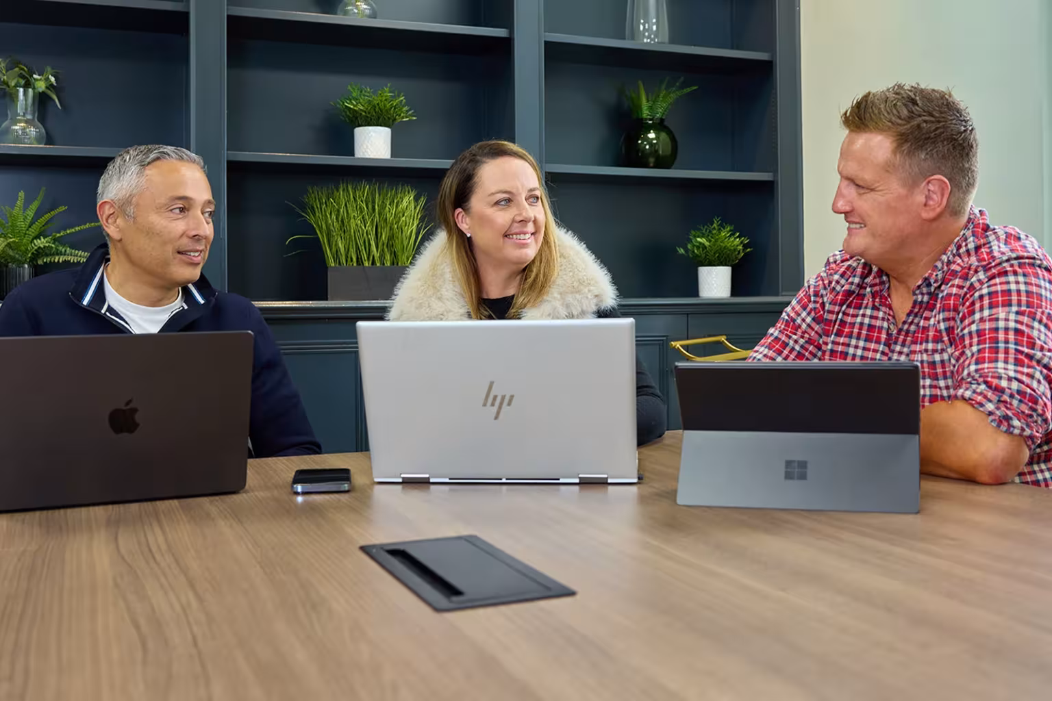 Three people smiling and talking together during a meeting with laptops.