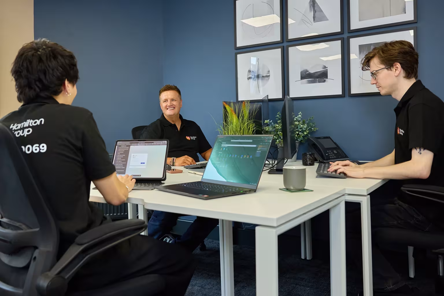 Hamilton Group team collaborating in a modern office with laptops and computers.