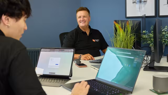 Two people collaborating at a table with laptops in a modern office.