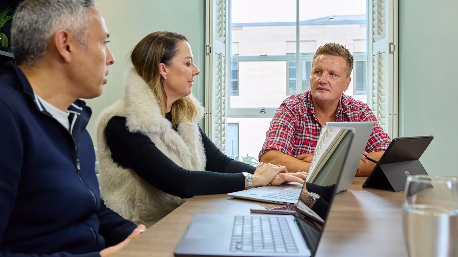Team in conversation around a meeting table with laptops in front of them.