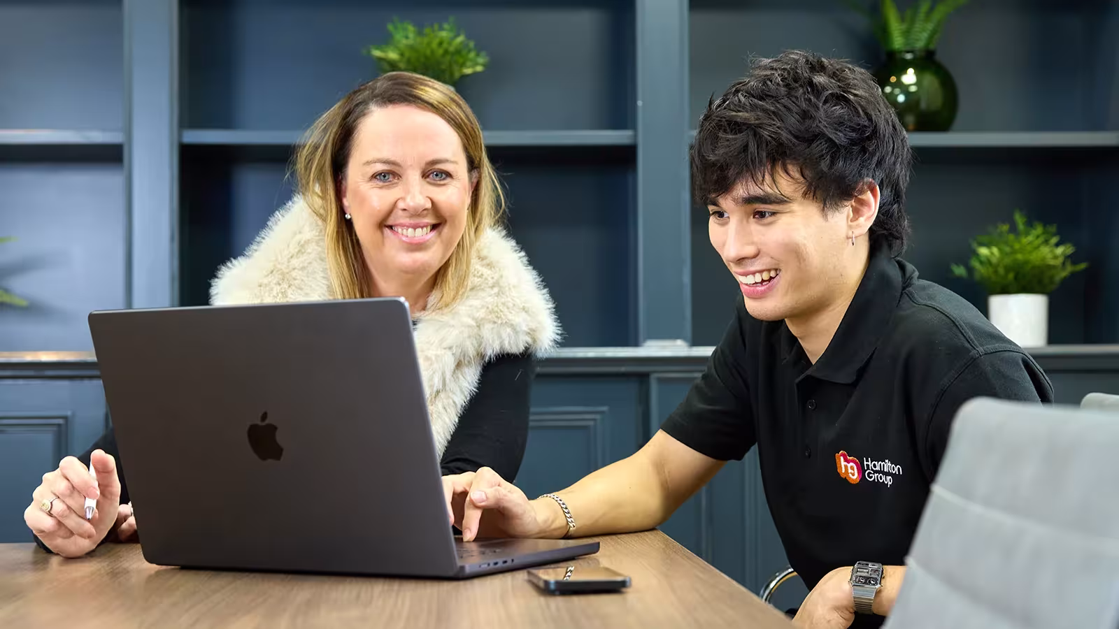 Two team members smiling while reviewing work on a laptop.