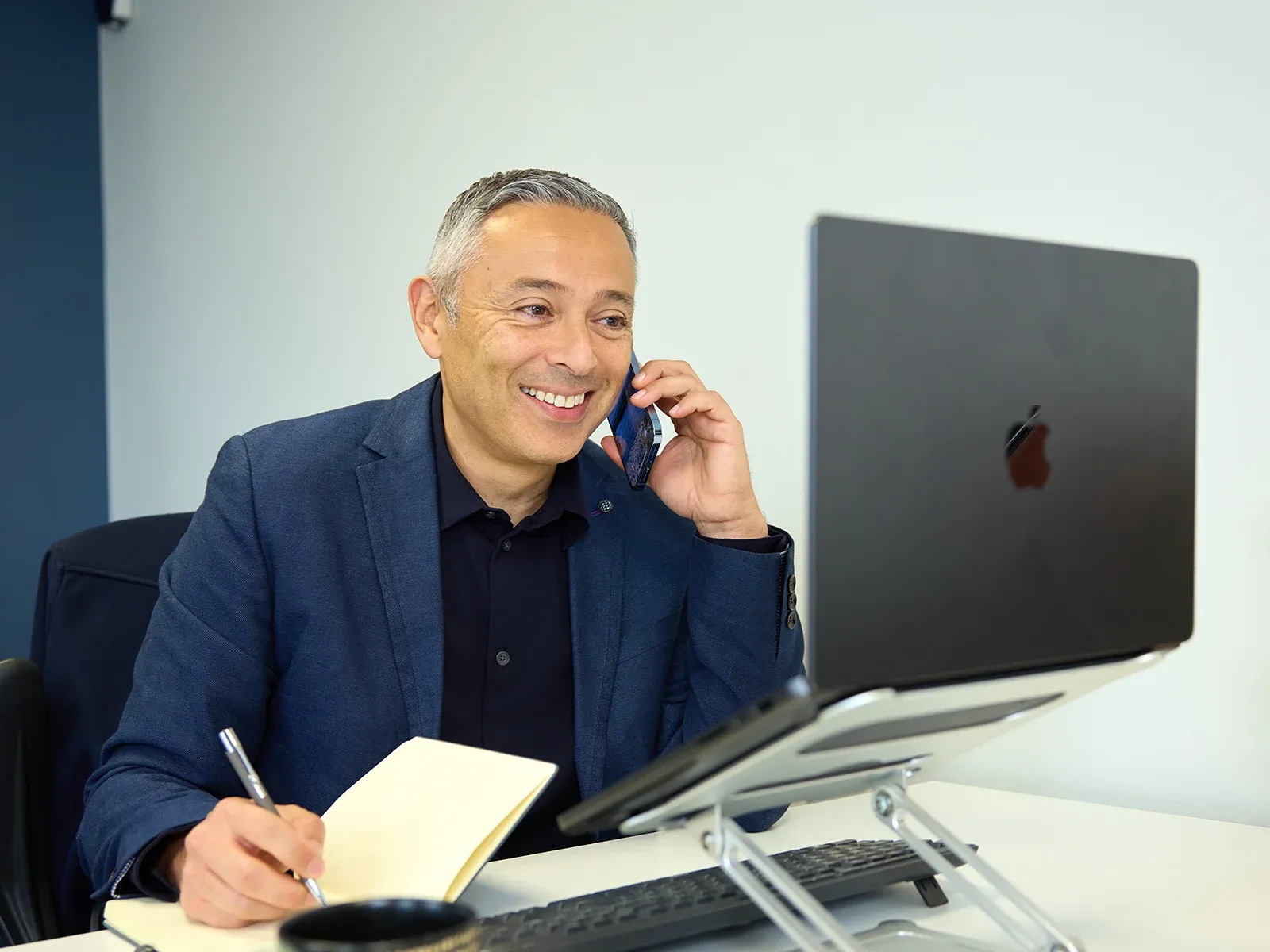 Business person taking notes during a phone call at their desk.