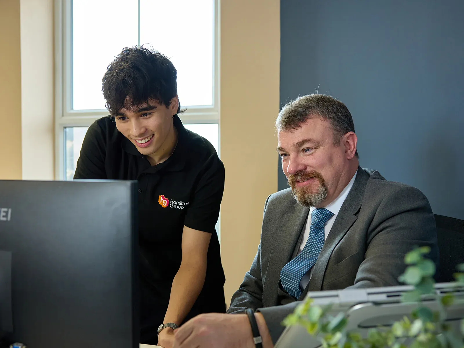 Hamilton Group team member assisting a colleague at a computer in the office.