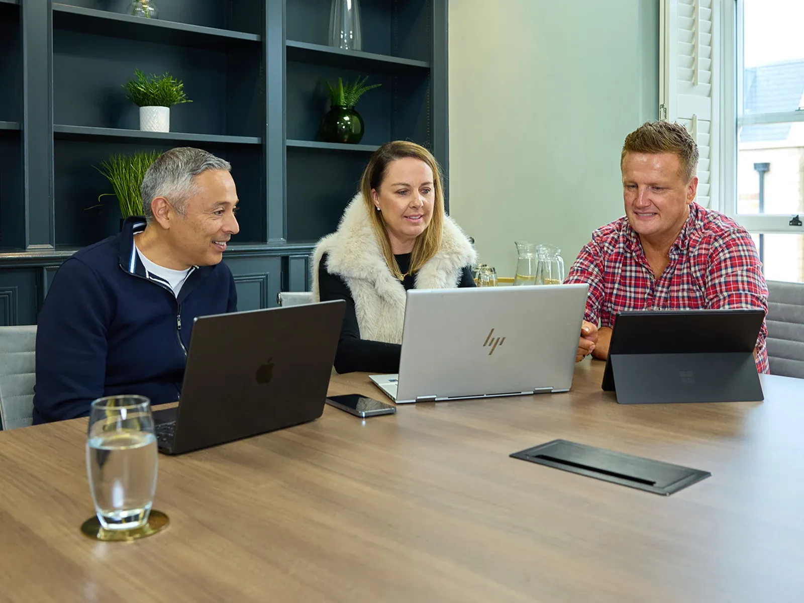 Three colleagues collaborating at a meeting table with laptops open.