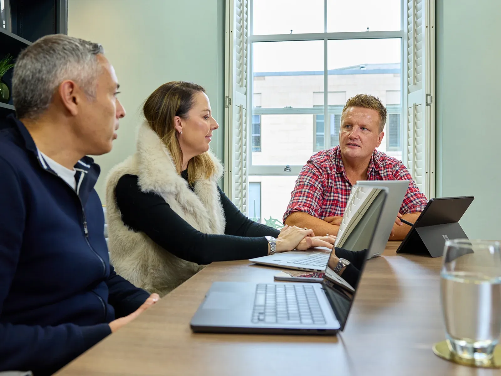 Team in conversation around a meeting table with laptops in front of them.