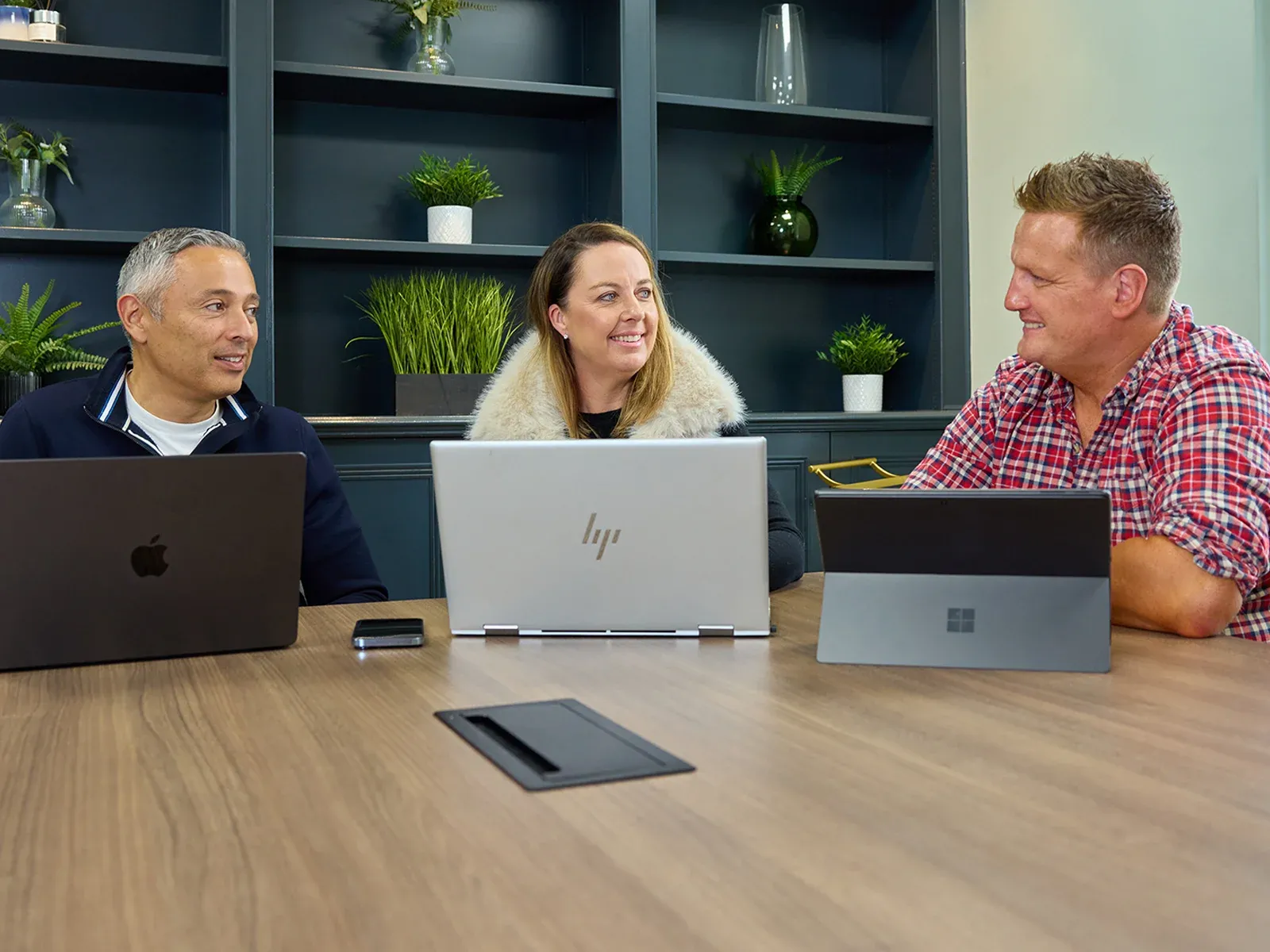 Three people smiling and talking together during a meeting with laptops.