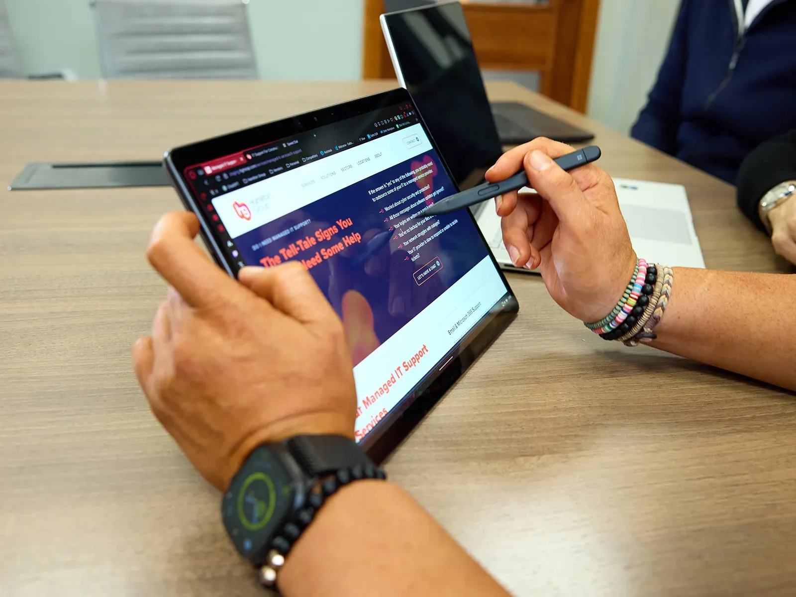 Person using a stylus to point at a tablet screen showing the Hamilton Group website.