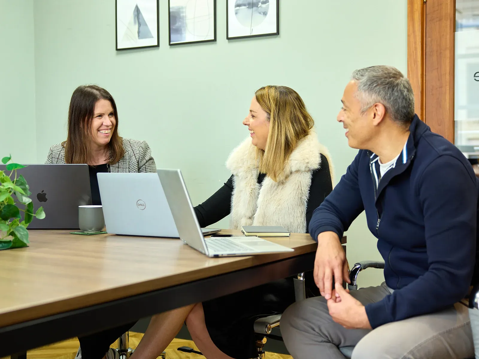 Three colleagues smiling and talking together during a meeting at a conference table.