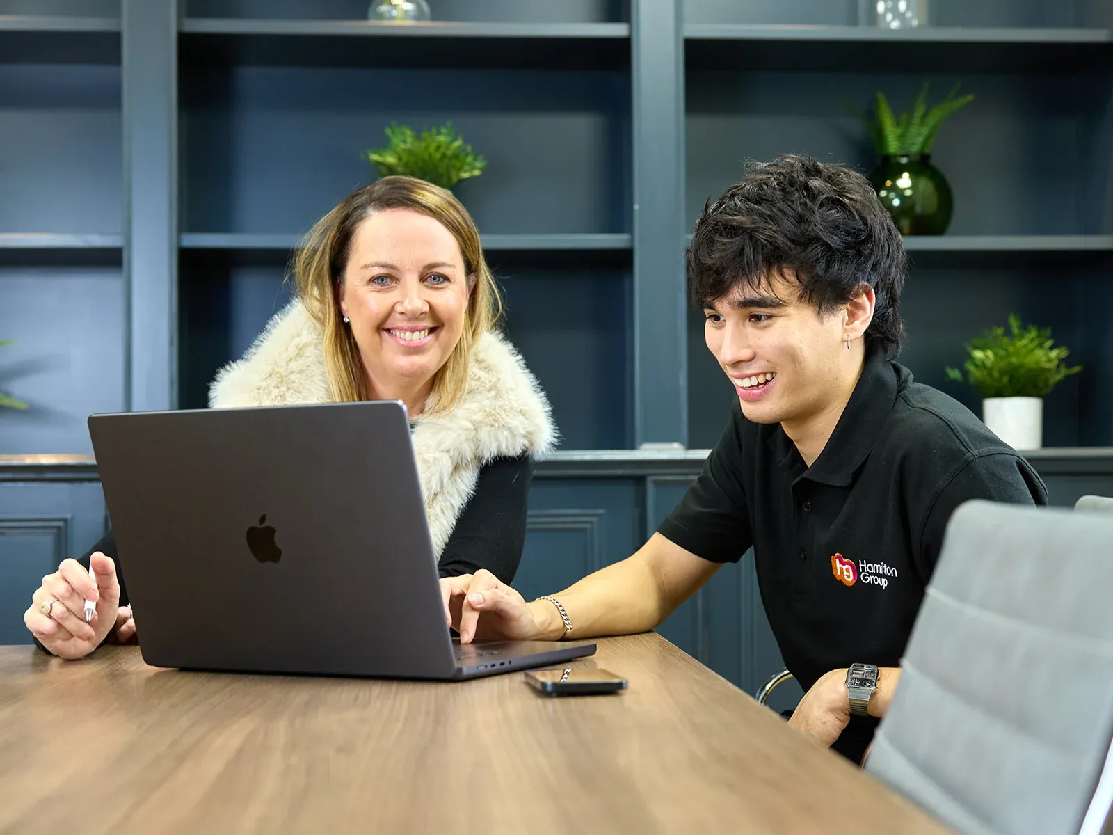 Two team members smiling while reviewing work on a laptop.