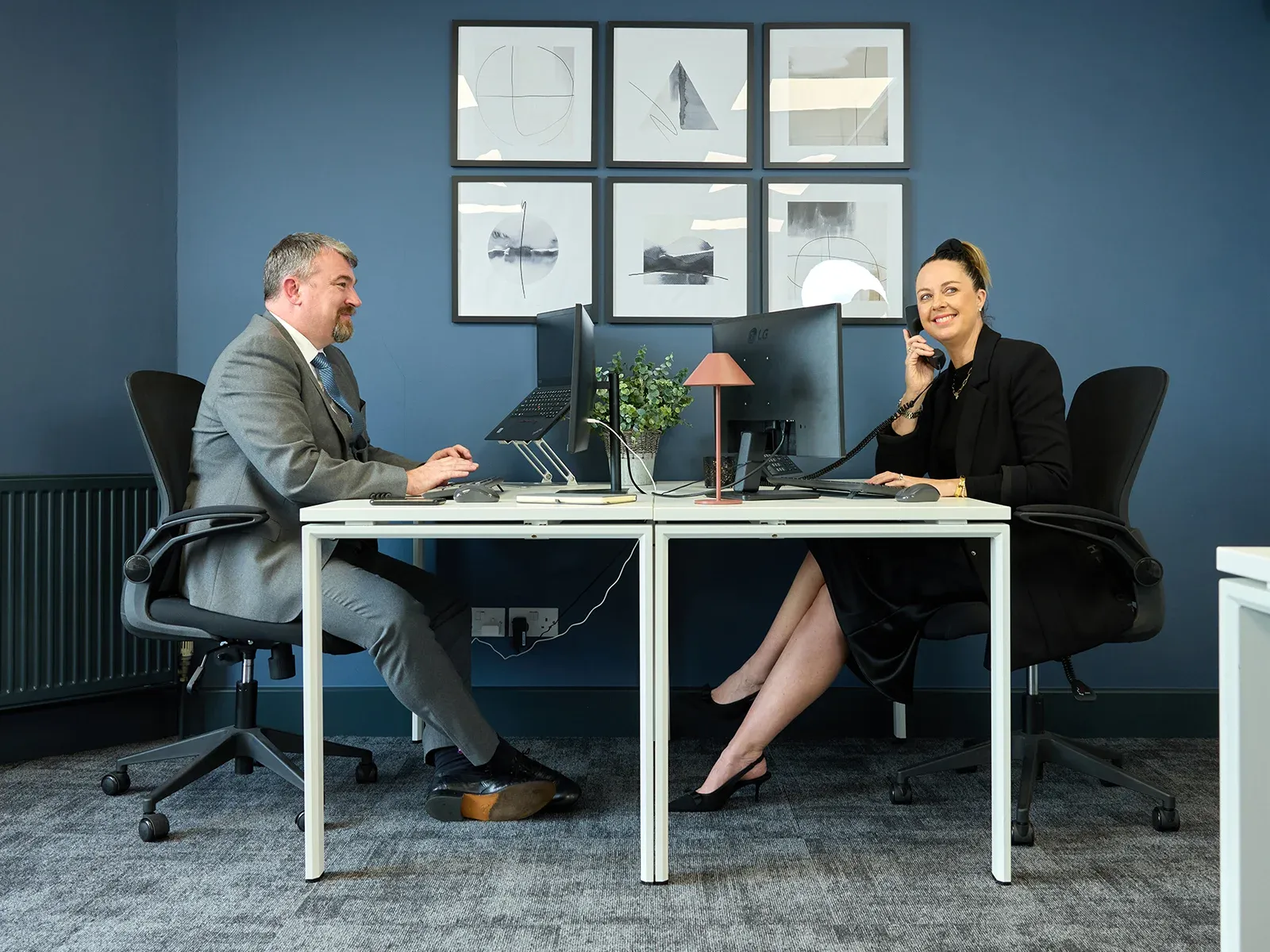 Two colleagues working side by side at desks in a modern office.