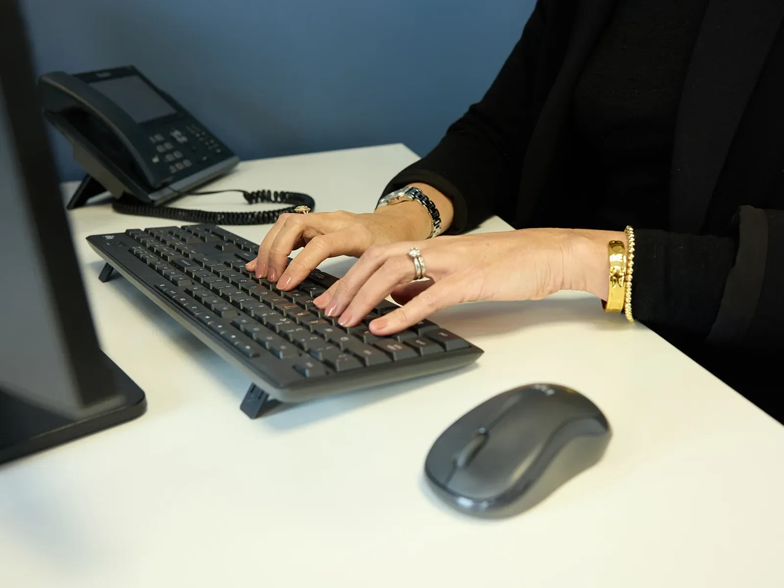 Hands typing on a keyboard at an office desk with a phone and monitor nearby.