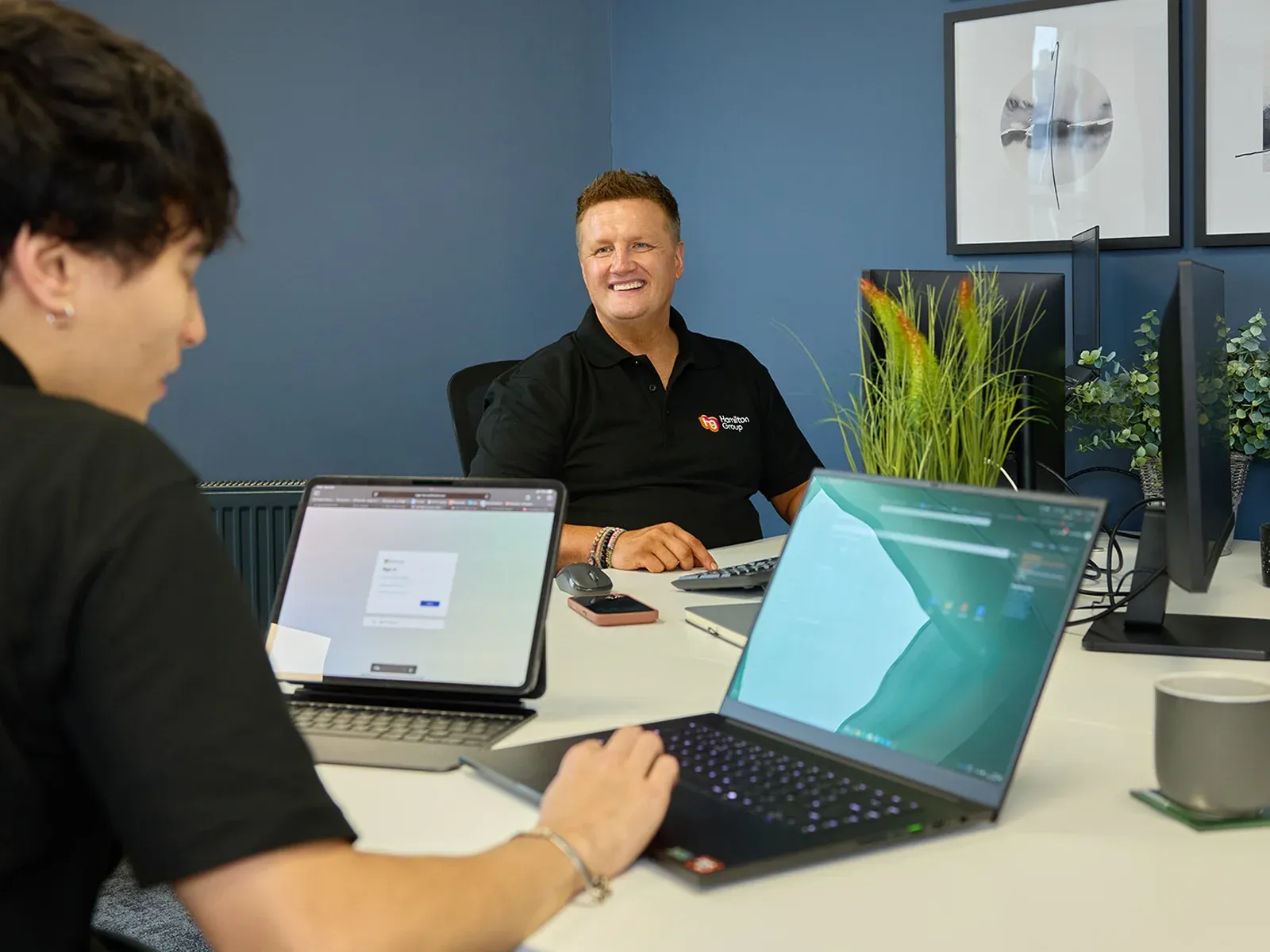 Two people collaborating at a table with laptops in a modern office.