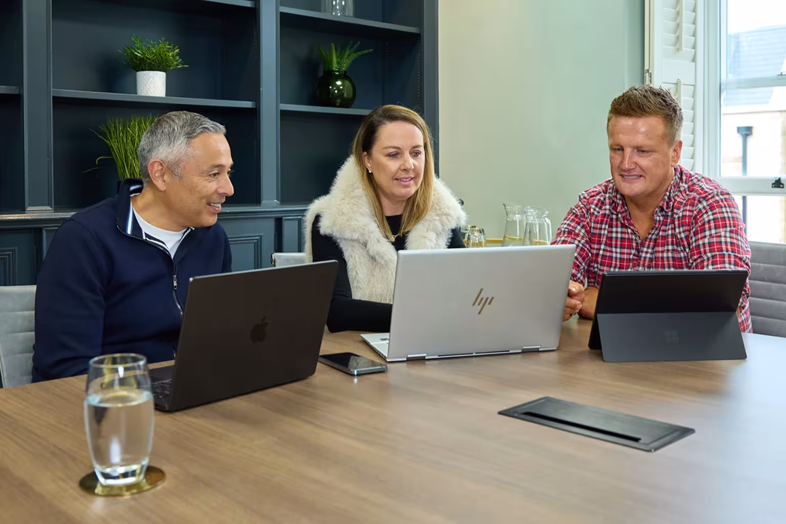 Three colleagues collaborating at a meeting table with laptops open.