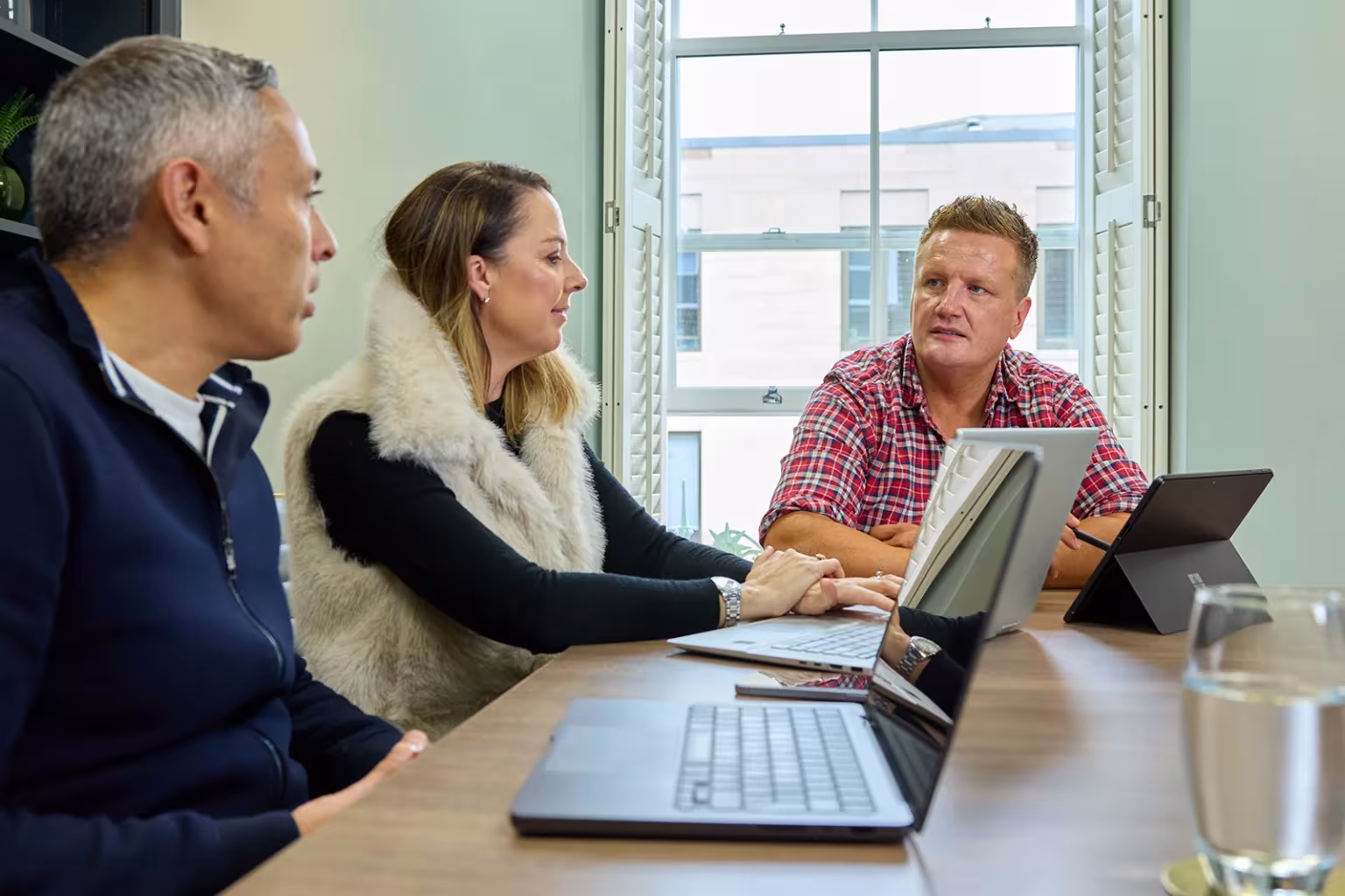 Team in conversation around a meeting table with laptops in front of them.